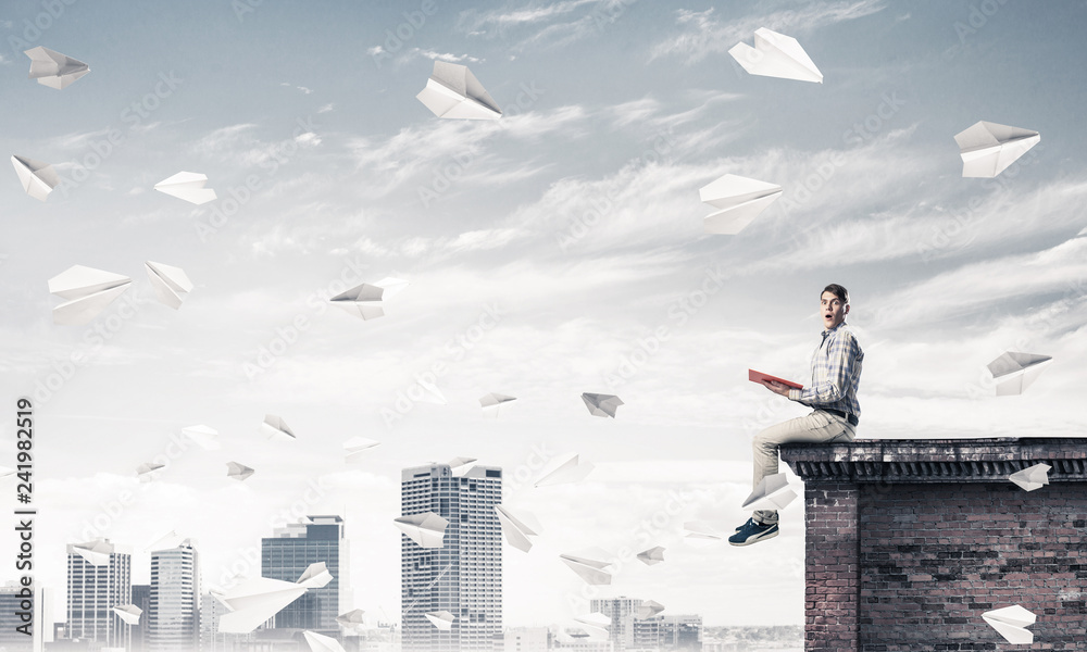Handsome student guy on roof edge reading book and paper planes Handsome student guy on roof edge reading book and paper planes