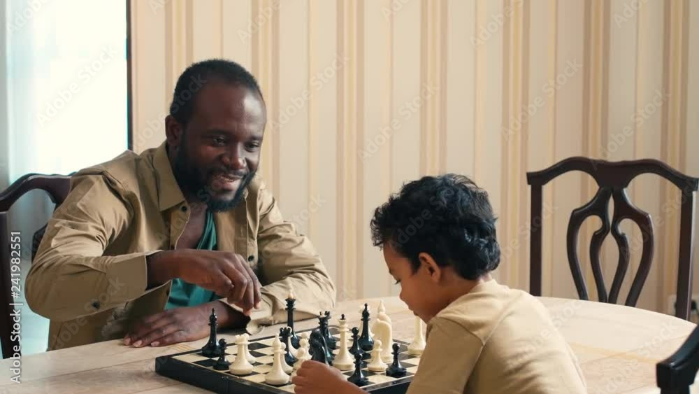 African American man explaining his son chess rules, showing figures and calling their names African American man explaining his son chess rules, showing figures and calling their names