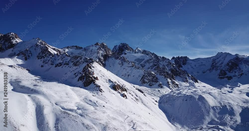 Snow-capped mountains. Shooting with the drone. White snow on gray and brown stones. Blue sky and light white clouds. The gorge is completely covered with snow. Panorama of nature. Highest mountain. Snow-capped mountains. Shooting with the drone. White snow on gray and brown stones. Blue sky and light white clouds. The gorge is completely covered with snow. Panorama of nature. Highest mountain.