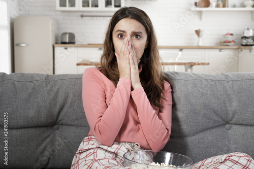 Fotografija European lady watching TV and looking frightened with round eyes, having seen so