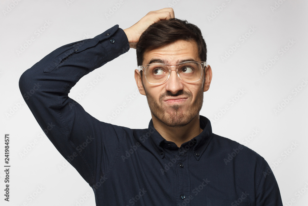 Caucasian man wearing glasses isolated on grey background scratching his head trying to find solution Caucasian man wearing glasses isolated on grey background scratching his head trying to find solution