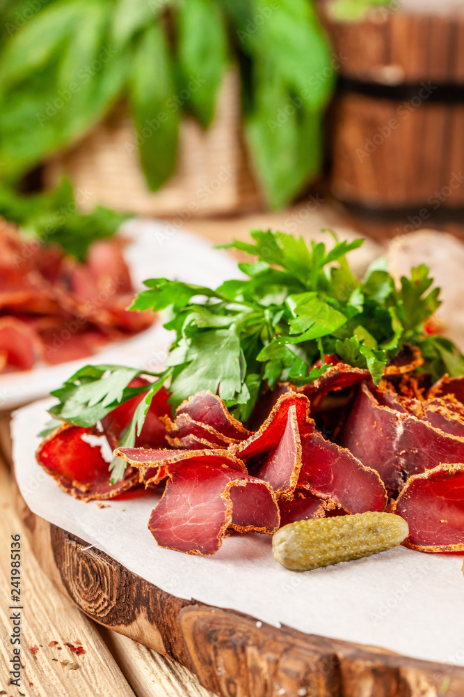 Concept of Georgian restaurant. A glass of black beer with foam stands on a wooden table, next to it is a beer snack, dried sausage, basturma, smoked meat and parsley with dill.