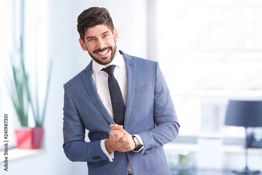 Handsome young businessman wearing suit and tie and looking at camera while stanading in the office Handsome young businessman wearing suit and tie and looking at camera while stanading in the office