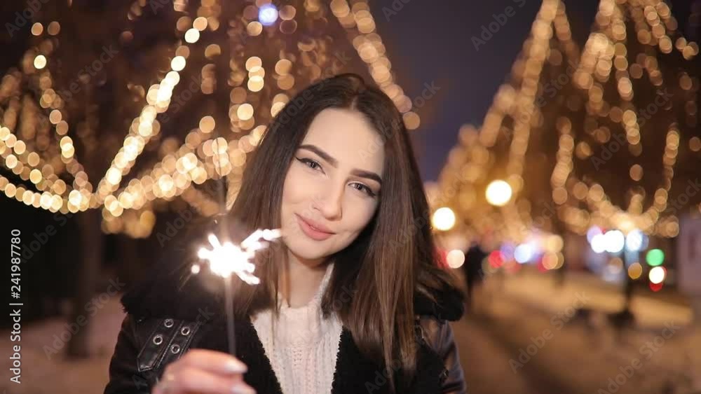 Woman walking along wonderful night alley with garlands holding sparklers Woman walking along wonderful night alley with garlands holding sparklers
