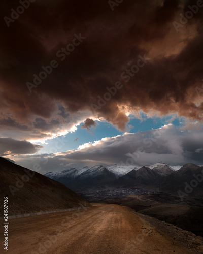 Dirt road leading to mountains and dark clouds in background