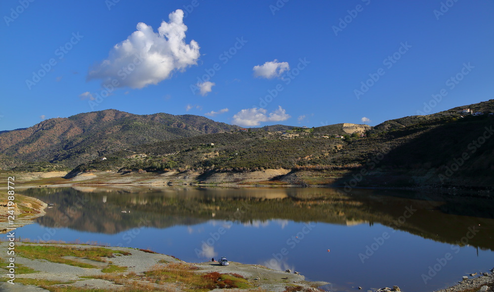 lake in the mountains, beautiful reflections in water, fisherman and his car, blue sky with nice white clouds