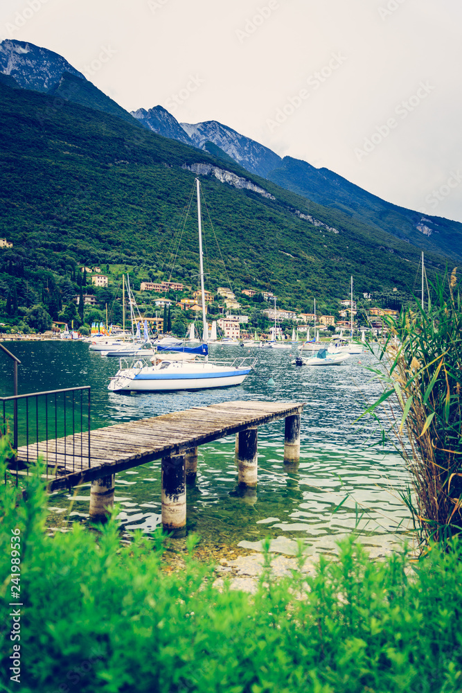 Wooden dock pier extending over blue lake water, sailing boats and mountains