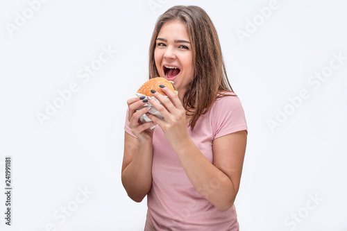 Happy young woman look on camera with mouth opened. She hold burger with both hands. Isolated on white background.