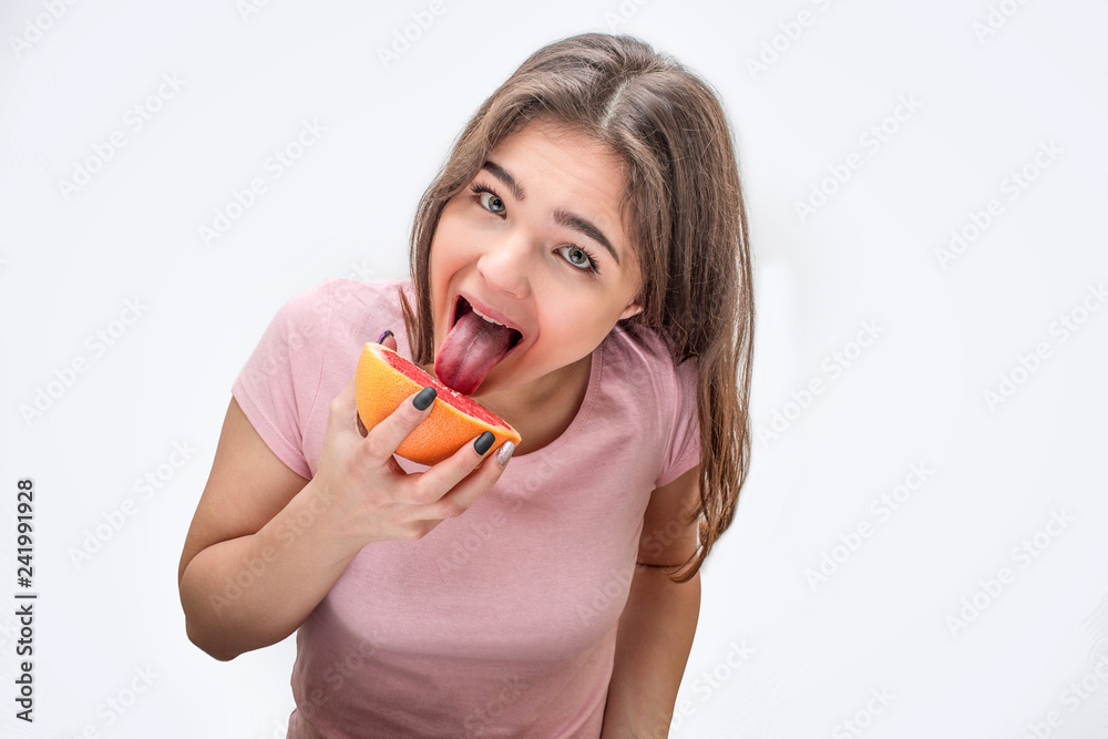 Funny young woman licks piece of grapefruit. She look straight. Isolated on white background. Funny young woman licks piece of grapefruit. She look straight. Isolated on white background.