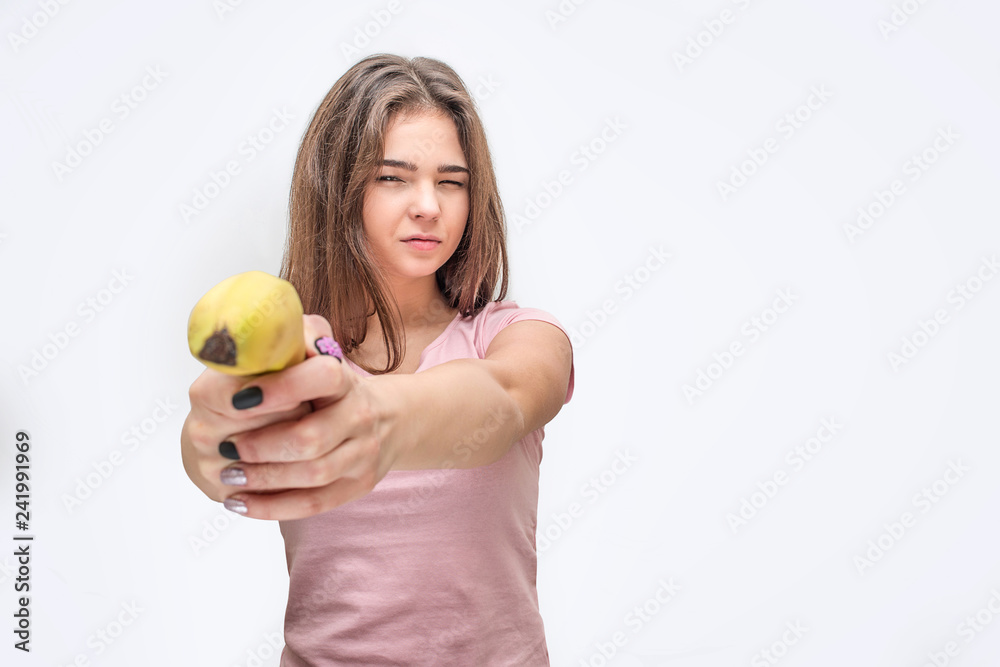 Serious young woman hold banana like gun. Isolated on grey background. Serious young woman hold banana like gun. Isolated on grey background.