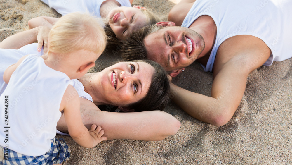 family lying on beach, top view.