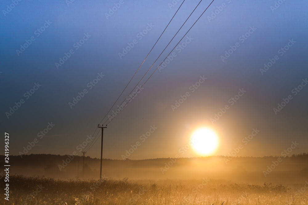 Dawn, the morning sun rises over the field and power transmission line, foggy dawn landscape, wires create lines