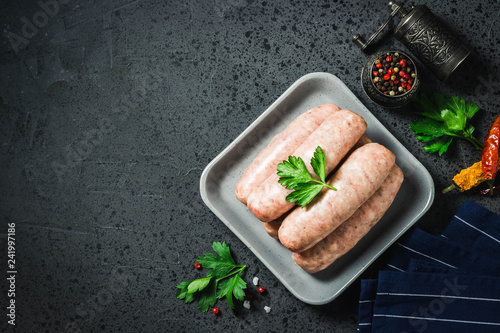 Raw sausages with herbs, spices, herbs on dark background. Top view, space for text.