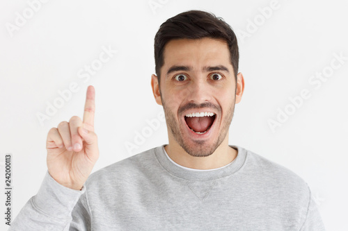 Portrait of excited young man looking at camera, smiling, pointing finger up if he has great idea