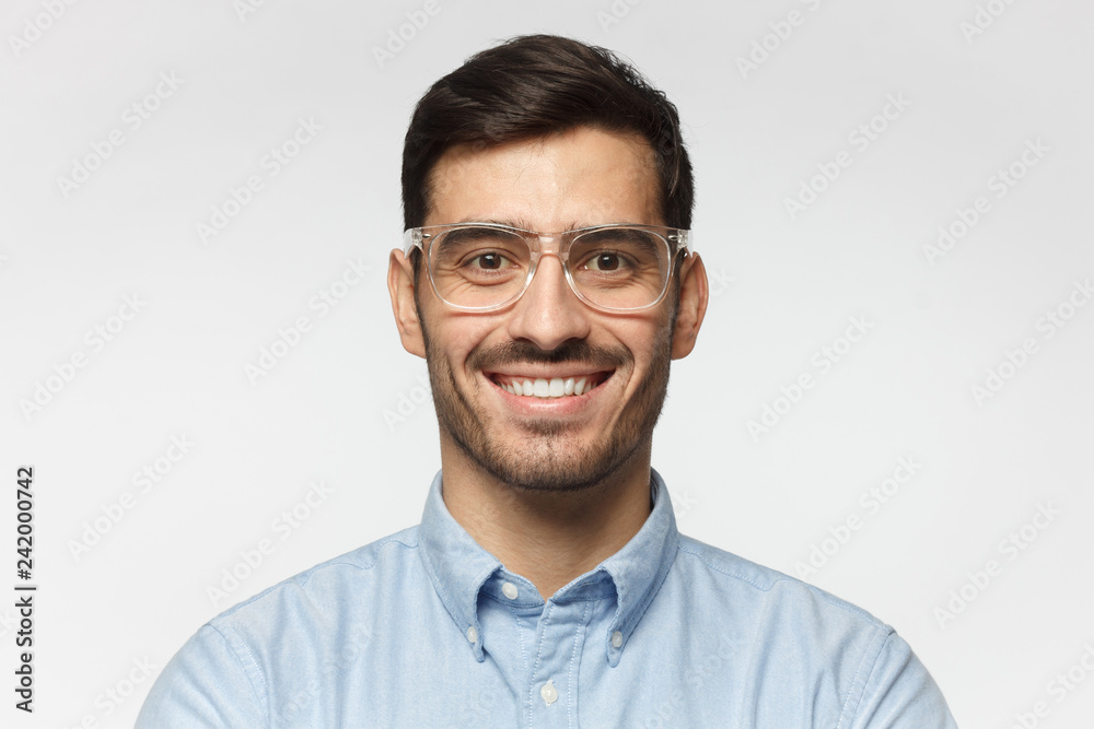 Smart businessman smiling at camera, wearing trendy transparent glasses, isolated on gray background Smart businessman smiling at camera, wearing trendy transparent glasses, isolated on gray background