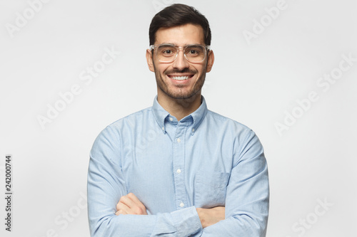 Handsome smiling business man in blue shirt standing with crossed arms, isolated on gray background