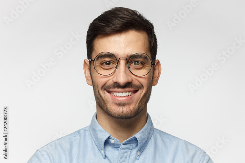 Portrait of businessman smiling at camera, wearing round glasses, isolated on gray background