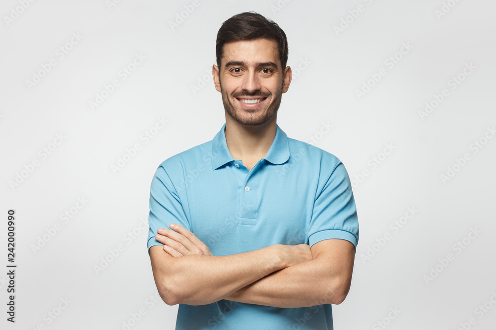 Smiling handsome man in blue polo shirt standing with crossed arms isolated on gray background - obrazy, fototapety, plakaty 