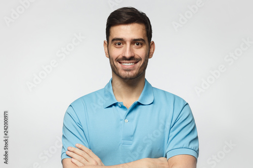Portrait of smiling handsome man in blue polo shirt, standing with crossed arms isolated on grey background © Damir Khabirov
