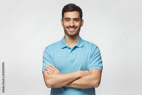 Smiling handsome man in blue polo shirt standing with crossed arms isolated on gray background photo