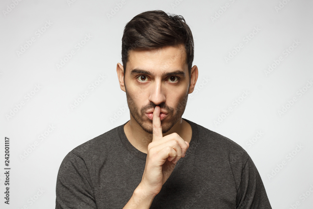 © Damir Khabirov - Young man dressed in casual t-shirt, pressing finger to lips as if asking to keep silence, isolated on gray background. Shhh gesture © Damir Khabirov - Young man dressed in casual t-shirt, pressing finger to lips as if asking to keep silence, isolated on gray background. Shhh gesture
