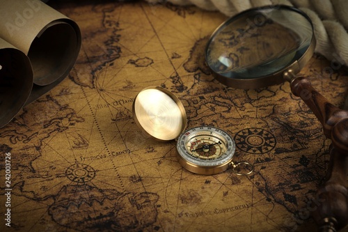 
Vintage Compass and magnifying glass lies on an ancient world map - adventure stories background