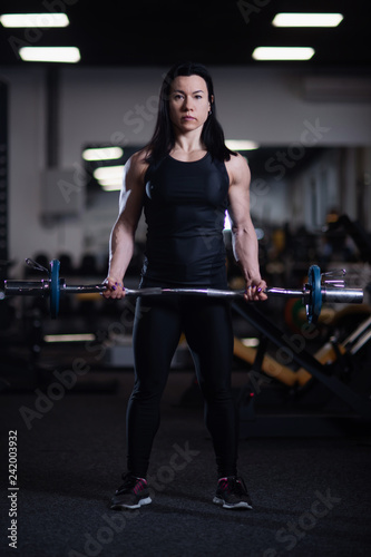 fitness girl trains biceps with barbell in the gym.