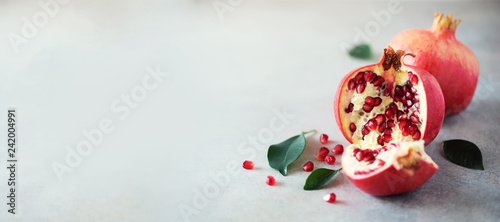 Ripe pomegranate fruit with green leaves on grey concrete background. Banner with copy space. Vegan, healthy diet concept