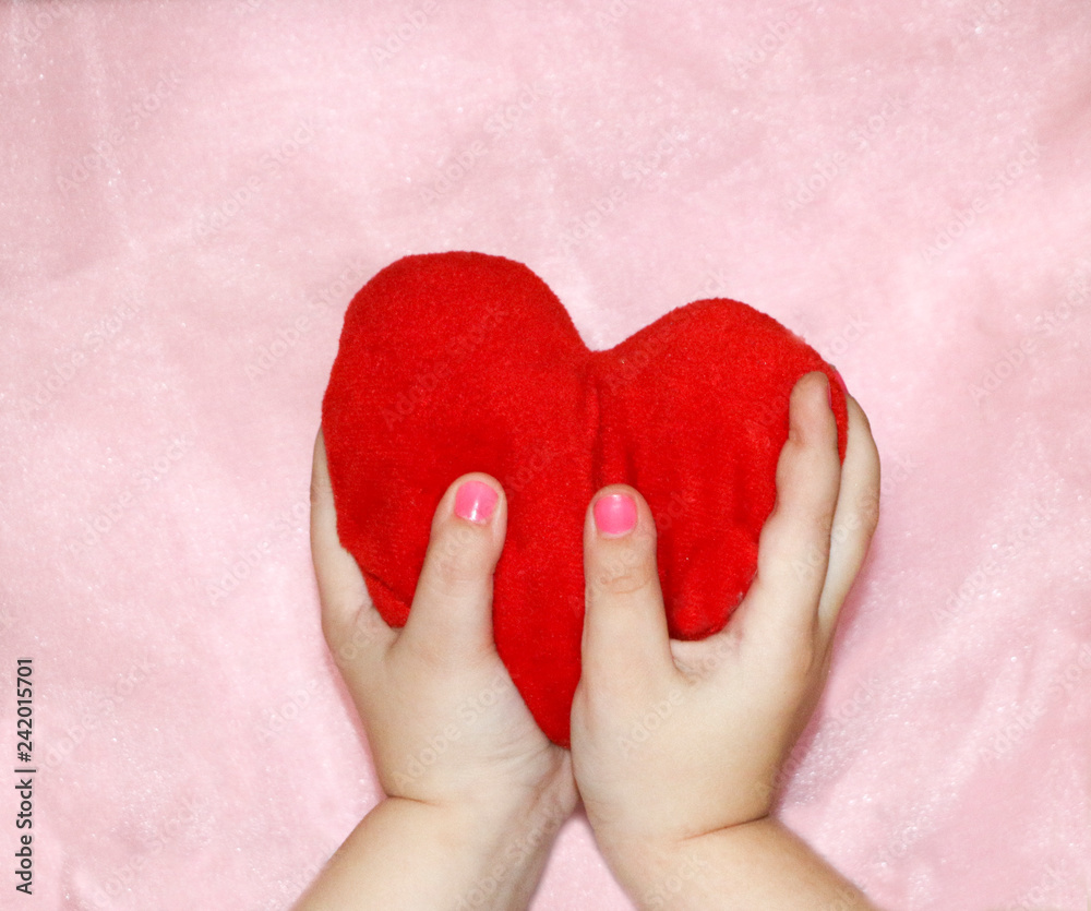 soft red heart in the hands of a child on a pink background