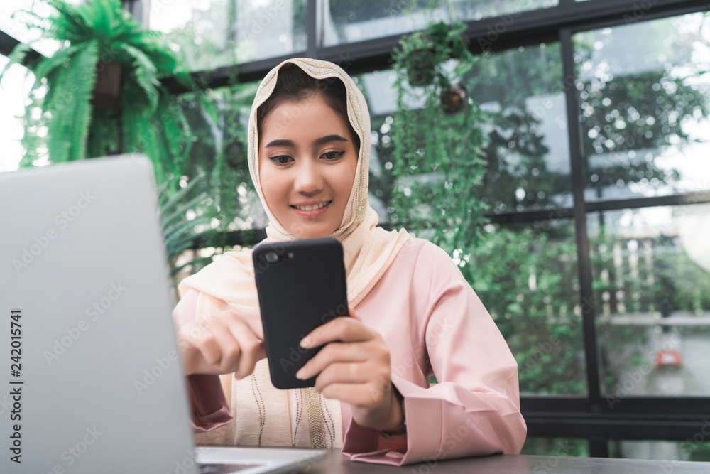 Beautiful young smiling asian muslim woman working on phone sitting in living room at home. Asian business woman working document finance and calculator in her home office. Enjoying time at home. Beautiful young smiling asian muslim woman working on phone sitting in living room at home. Asian business woman working document finance and calculator in her home office. Enjoying time at home.