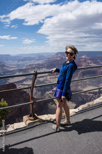 Female tourist stands close to the edge railing at an overlook at Grand Canyon National Park in Arizona