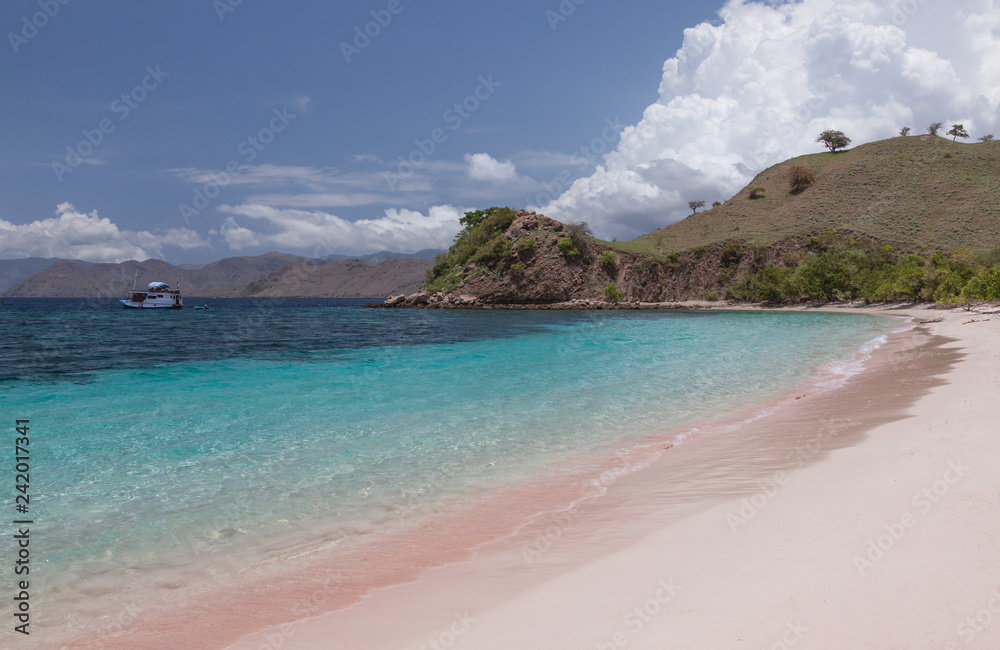 Pink beach with crystal clear water and a boat near tropical islands