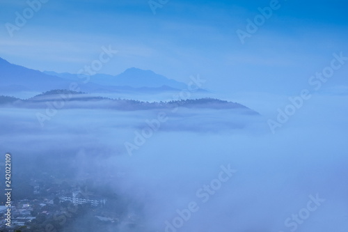 Top view misty morning above Mae Hong Son City, view of the sea of mist moving above city around with mountain and cloudy sky background, sunrise at Wat Phra That Doi Kong Mu, Mae Hong Son Thailand.