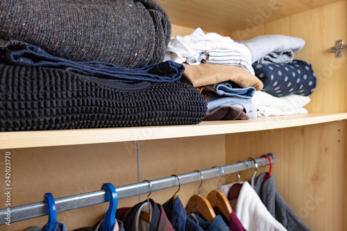 Wardrobe shelf with abundance of clothes. Consumerism concept: organised and layered personal things in a wooden closet