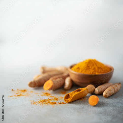 Turmeric powder in wooden bowl and fresh turmeric root on grey concrete background. Banner with copy space. Square crop