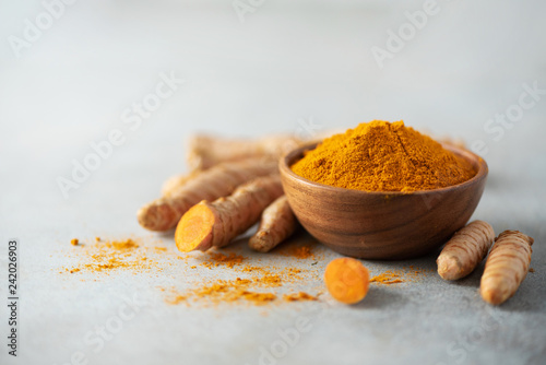 Turmeric powder in wooden bowl and fresh turmeric root on grey concrete background. Banner with copy space photo
