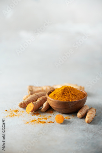Turmeric powder in wooden bowl and fresh turmeric root on grey concrete background. Banner with copy space