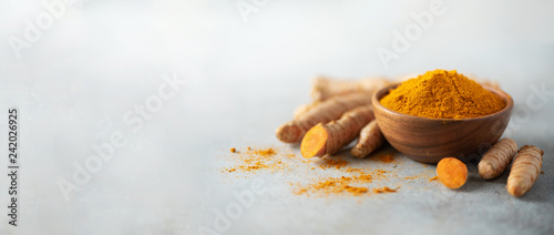 Turmeric powder in wooden bowl and fresh turmeric root on grey concrete background. Banner with copy space