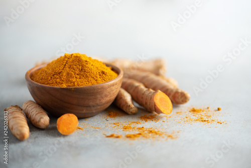 Turmeric powder in wooden bowl and fresh turmeric root on grey concrete background. Banner with copy space photo