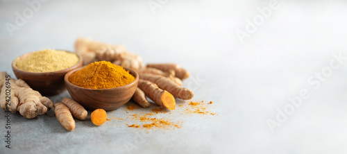 Turmeric and giger powder in wooden bowl and fresh turmeric root on grey concrete background. Banner with copy space photo