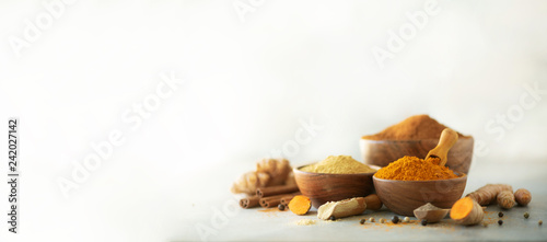 Ingredients for hot ayurvedic drink. Turmeric powder, curcuma root, cinnamon, ginger, lemon over grey background. Copy space, square crop. Spices for alternative medicine