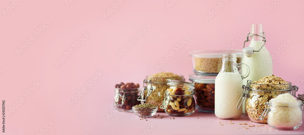 Fotografie Glass bottles of vegan plant milk and almonds, nuts, coconut, hemp seed milk on pink background
