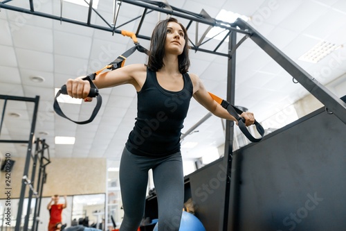 Young fitness woman doing exercises using the straps system in the gym. Sport, fitness, training, people concept.