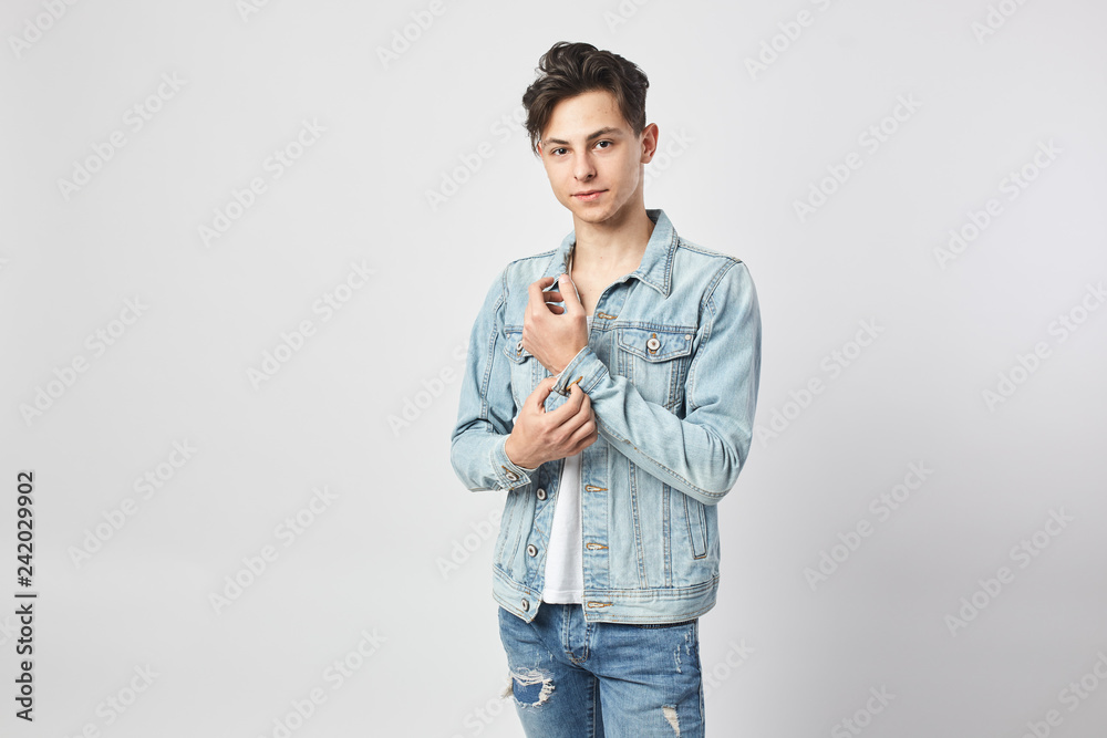 Φωτογραφία Young dark-haired guy in a white t-shirt, jeans and a denim jacket stands on the