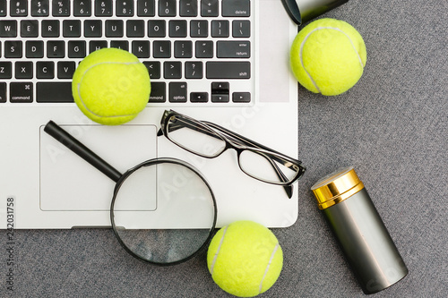 Top view of laptop, Sports Equipment, Tennis ball, Shuttlecock, glasses aon the Sports administration gray table.Business concept.