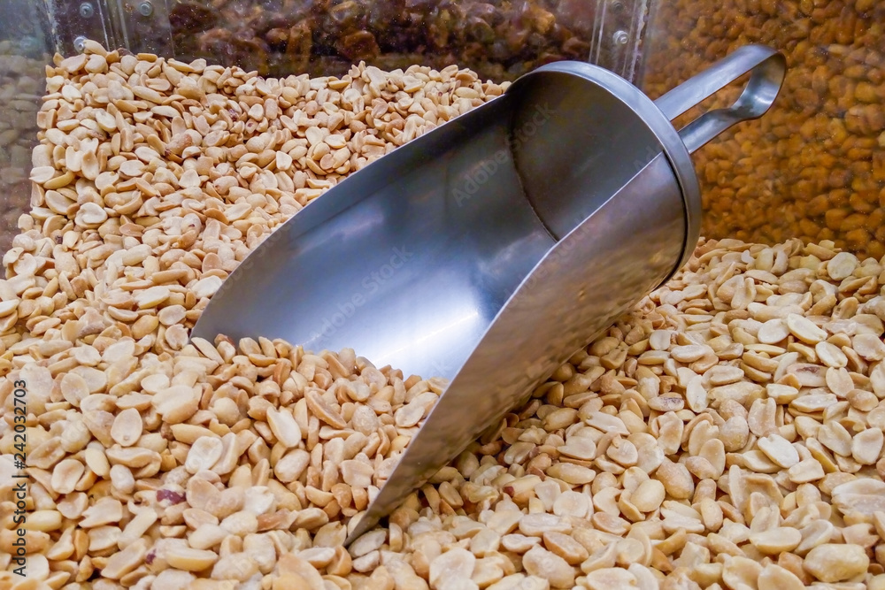 A pile of roasted peeled peanuts with metal scoop on the counter in supermarket A pile of roasted peeled peanuts with metal scoop on the counter in supermarket