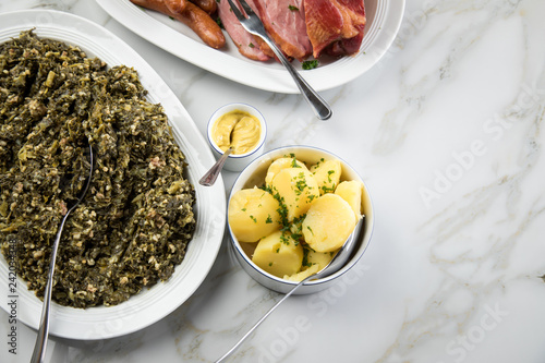 Oldenburger Grünkohl, Kassler Nacken, Kohlwurst und Pinkel auf Platten mit Kartoffeln und Senf auf Marmor Tisch