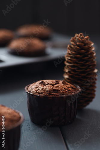 Hygge winter dessert. Homemade chocolate muffins and fir cone on dark background