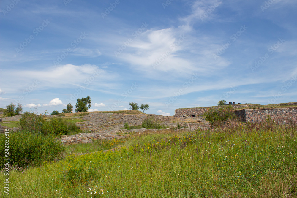The old granite walls of fortifications on Suomenlinna island are overgrown with grass on a summer sunny day in Finland.