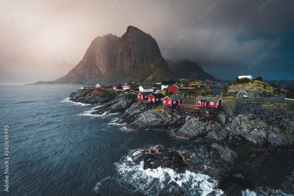 Sunset Panorama of famous tourist attraction Hamnoy fishing village on Lofoten Islands near Reine, Norway with red rorbu houses in autumn with clouds and blue sky and ocean waves.